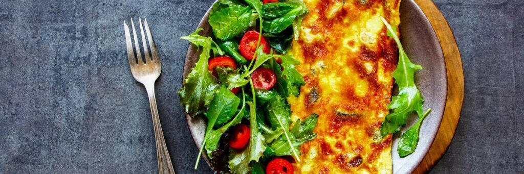 Jak krok po kroku przygotować omlet wysokobiałkowy? 2 Omlet złożony na pół i sałatka obok. Obrazek w artykule Jak krok po kroku przygotować omlet wysokobiałkowy?